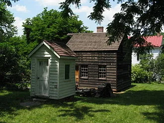 Two restored structures on the grounds of Historic Richmond Town: a relocated c. 1860 outhouse or privy, and a c. 1830-1860 Carpenter Shop reconstruction